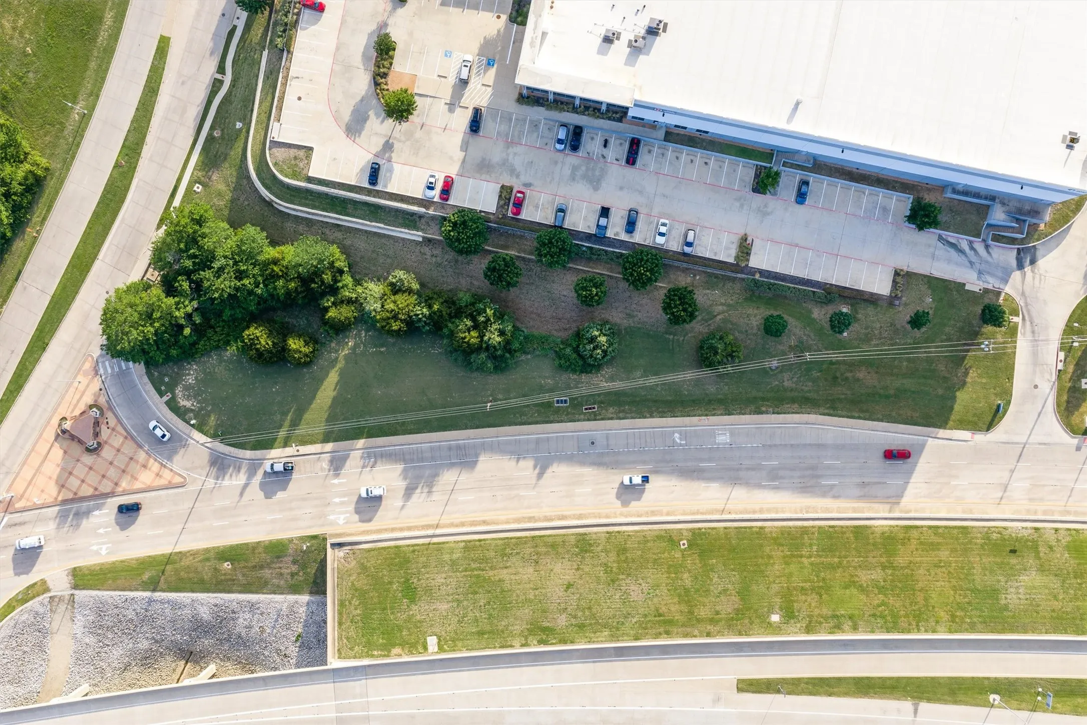 Expansive commercial property featuring a large structure, extensive parking area, multiple access roads, manicured green spaces, and mature trees