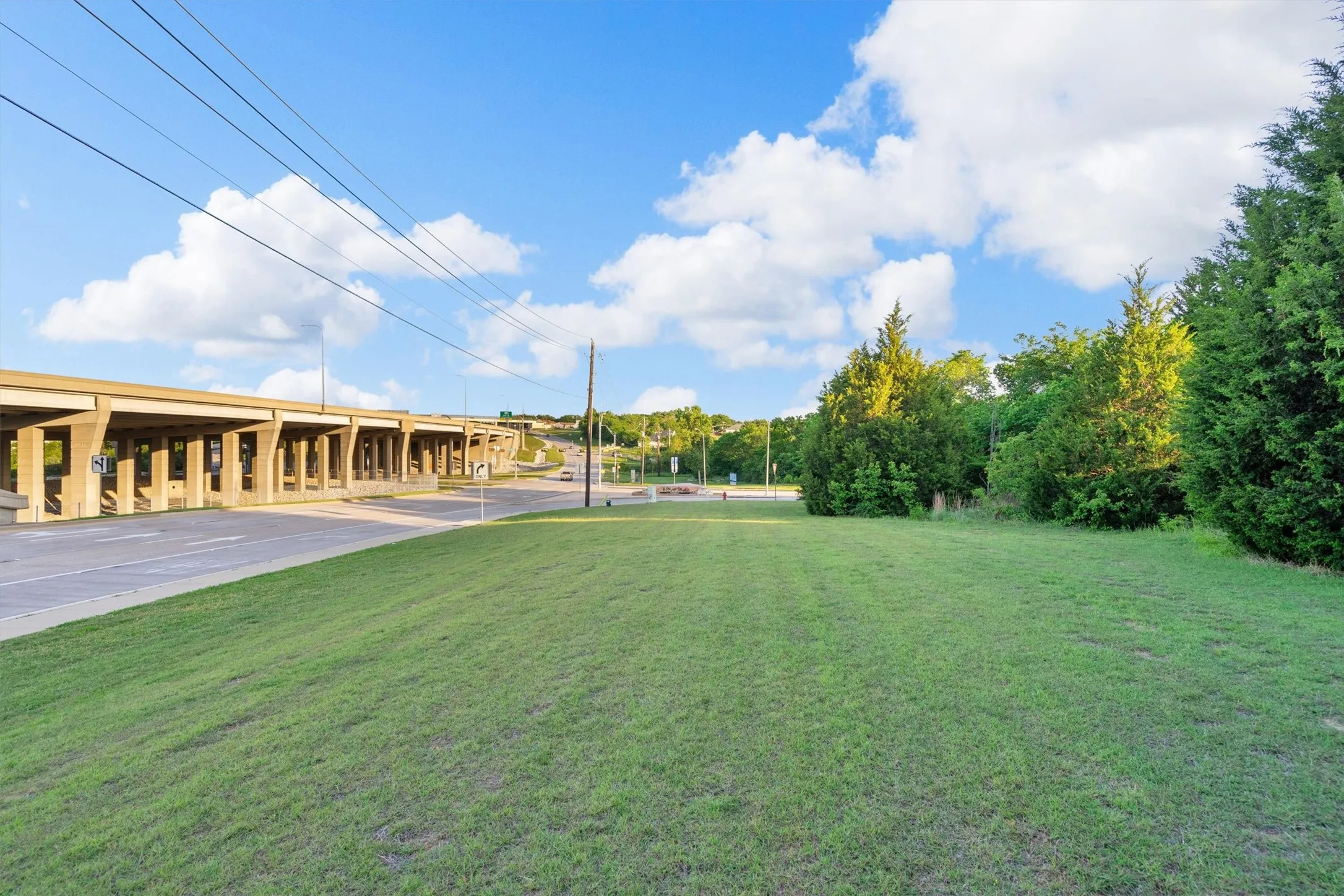 Expansive grass lot bordered by mature trees and multi-level highway infrastructure