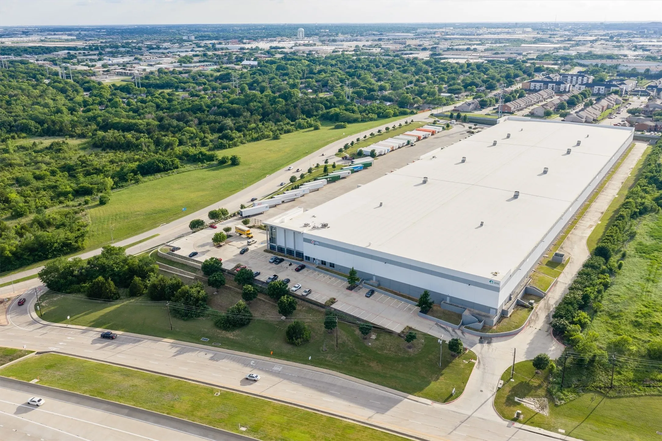 Large-scale commercial building featuring a white roof, expansive paved parking areas, and multiple loading docks