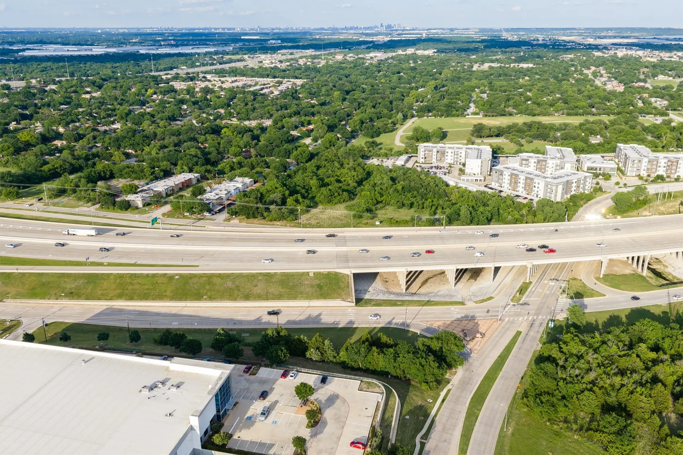 Aerial perspective showcasing a multi-lane highway overpass with surrounding green spaces, commercial structures, and residential buildings