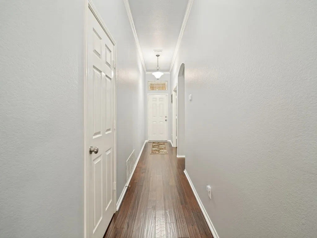 Hallway with wood-finish flooring, light gray walls, and white crown molding