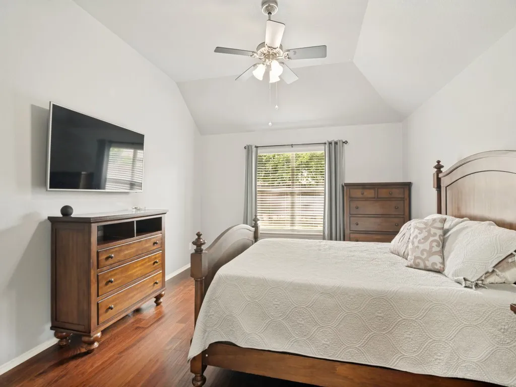 Bedroom featuring a vaulted ceiling with a ceiling fan, wood-finish flooring, and a window with blinds and drapes