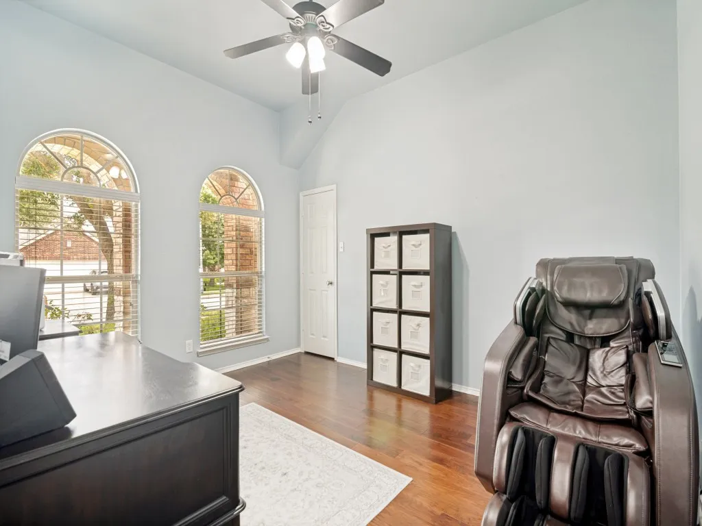 Vaulted ceiling room featuring two arched windows with blinds, dark wood-finish flooring, and a ceiling fan with light fixture