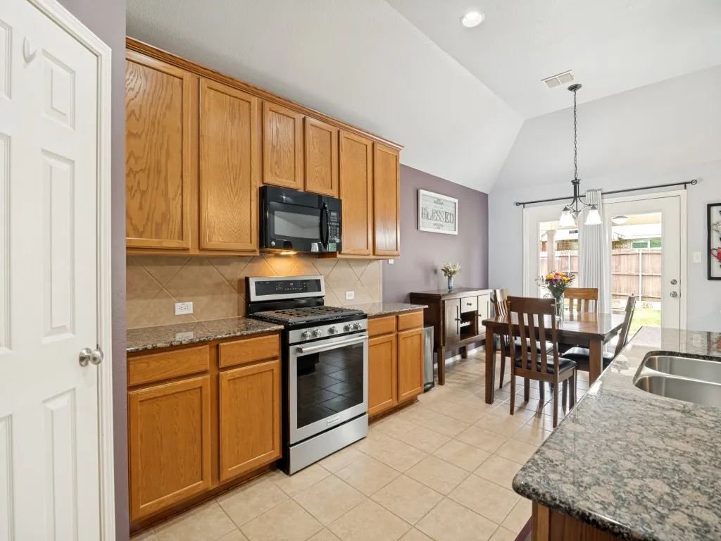 Kitchen featuring wood cabinetry, granite countertops, stainless steel gas range, over-range microwave, and tile flooring