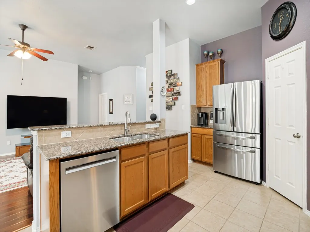 Kitchen island featuring a double-basin stainless steel sink, integrated dishwasher, and granite-look countertop with tile backsplash