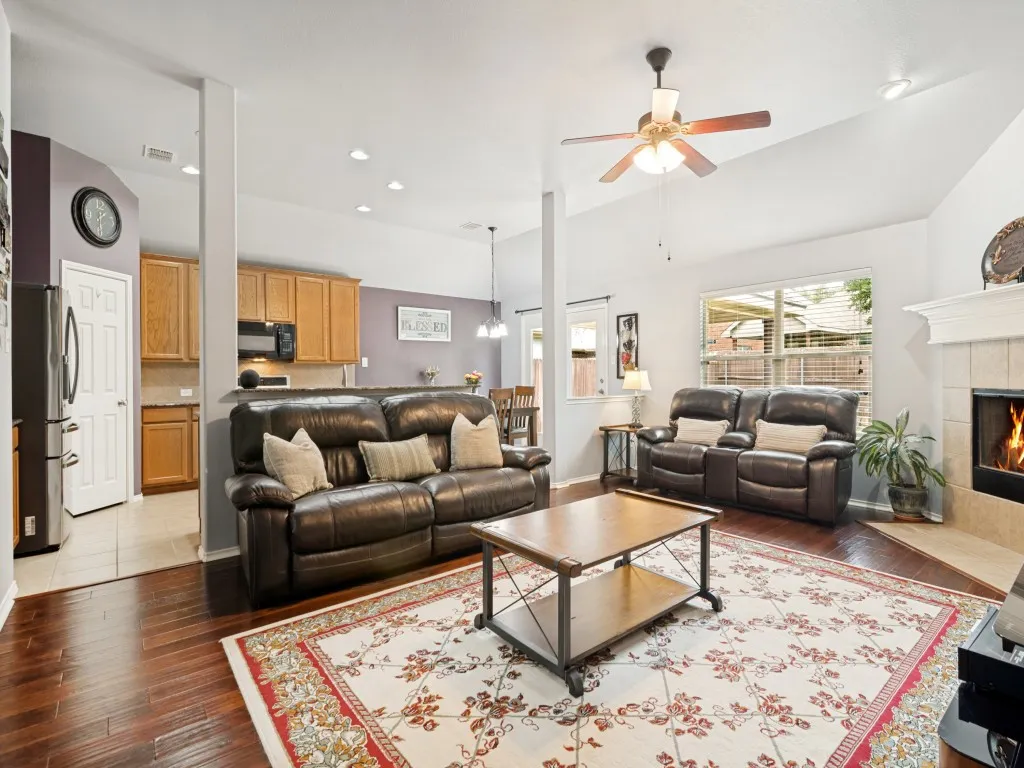 Living area featuring wood-finish flooring, a vaulted ceiling with a ceiling fan, recessed lighting, and a fireplace with a mantel and tile surround