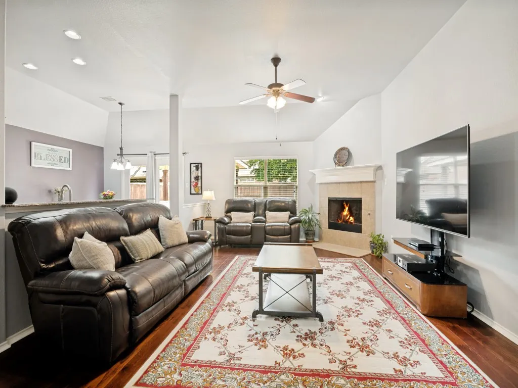 Spacious living area featuring wood-finish flooring, a vaulted ceiling, and a fireplace with a light-toned surround