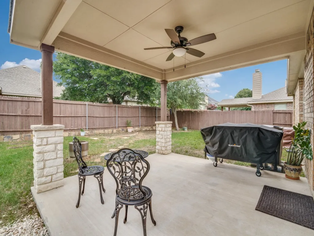 Covered concrete patio featuring a ceiling fan with integrated lighting, brick exterior wall, and stone-clad pillars