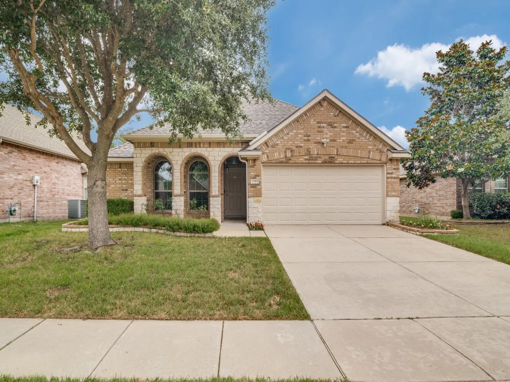Brick and stone facade residence featuring a two-car garage, arched windows, concrete driveway, and mature landscaping