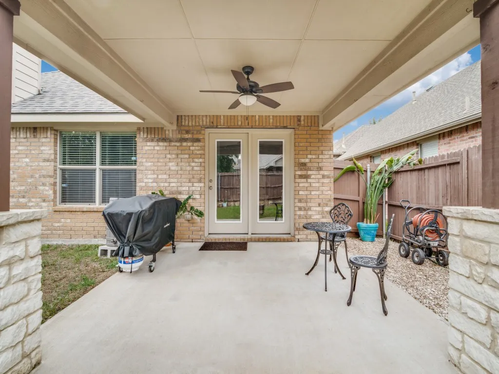 Covered concrete patio featuring a ceiling fan, dual glass panel doors, brick exterior, and a privacy fence