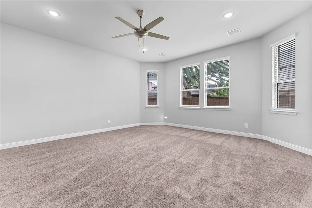 Spacious room featuring neutral carpet flooring, recessed lighting, a ceiling fan, and multiple windows with blinds