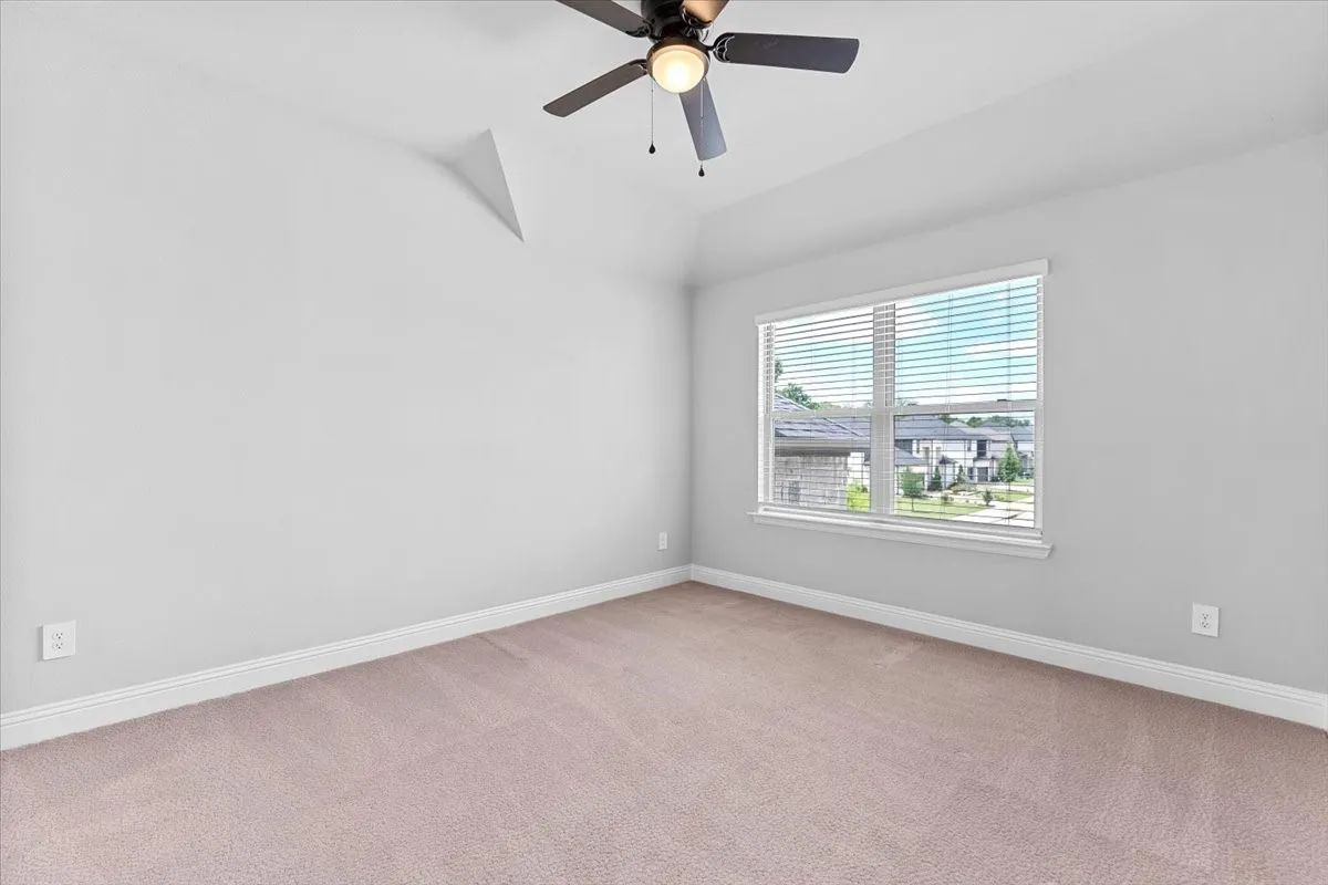 Carpeted interior room featuring a large window, a ceiling fan with integrated lighting, and a vaulted ceiling