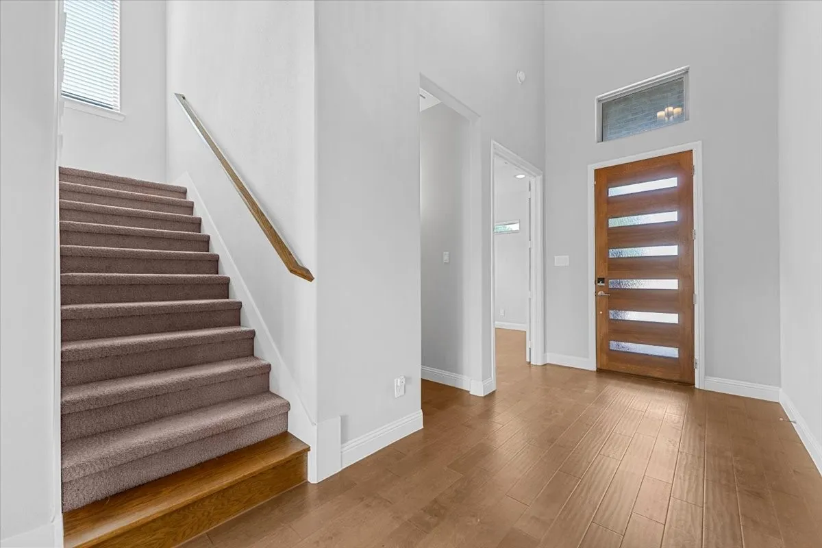 Entryway featuring high ceilings, wood-finish flooring, a modern wood door with frosted glass panels, and a carpeted staircase with wood risers and a wood handrail