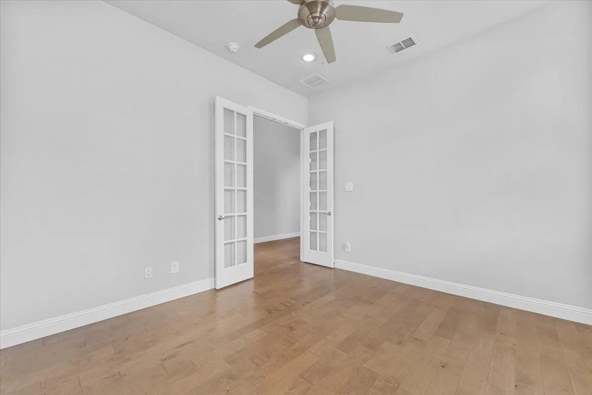 Room featuring French doors, wood-finish flooring, white baseboards, and a ceiling fan with integrated lighting