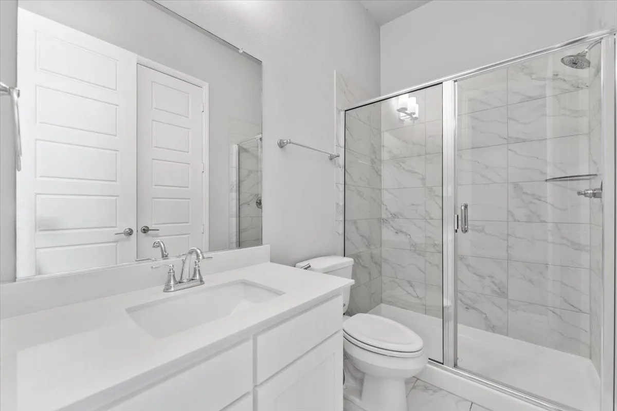 White vanity with integrated sink and chrome faucet, frameless mirror, and a glass-enclosed shower with tiled walls