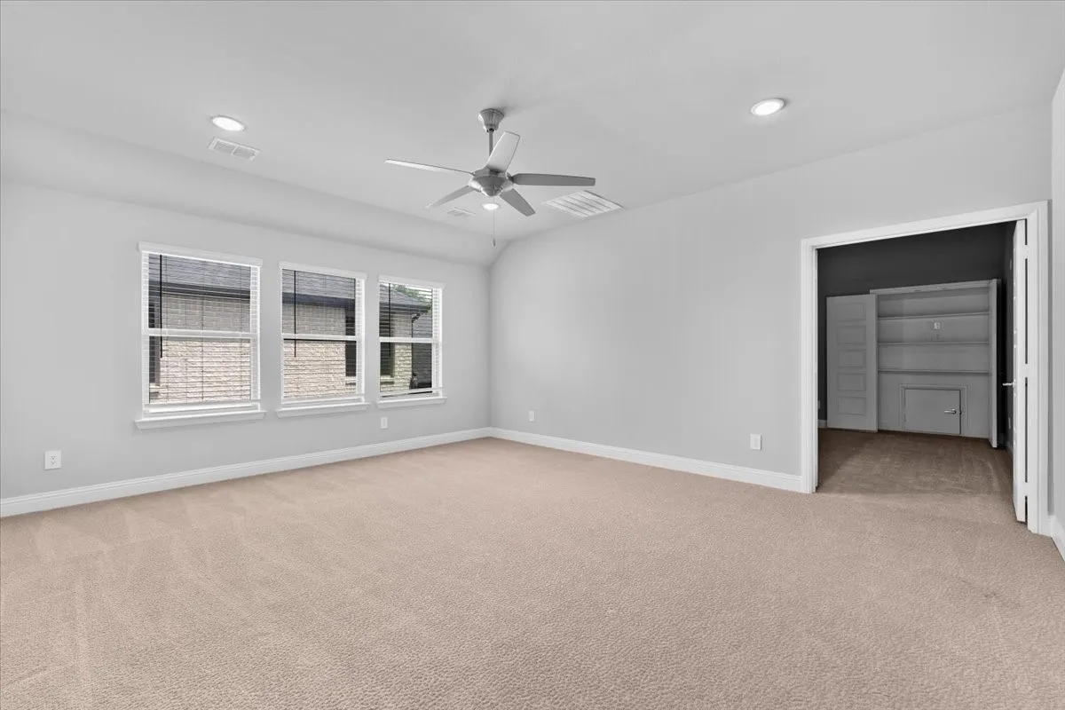 Spacious room with plush carpeting, three large windows, a ceiling fan, recessed lighting, and an open doorway revealing a built-in storage unit