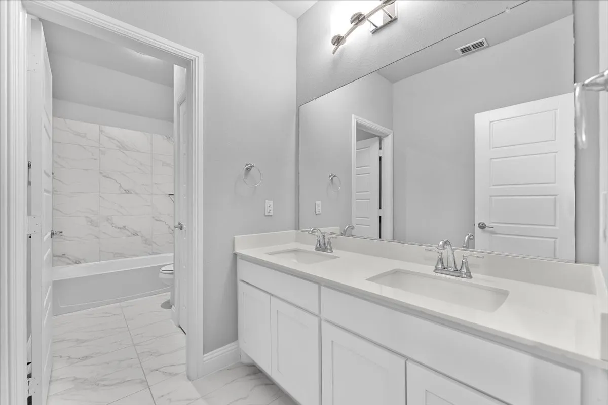 Bathroom featuring a dual vanity with white cabinetry and integrated sinks, a large wall-mounted mirror, and brushed nickel fixtures