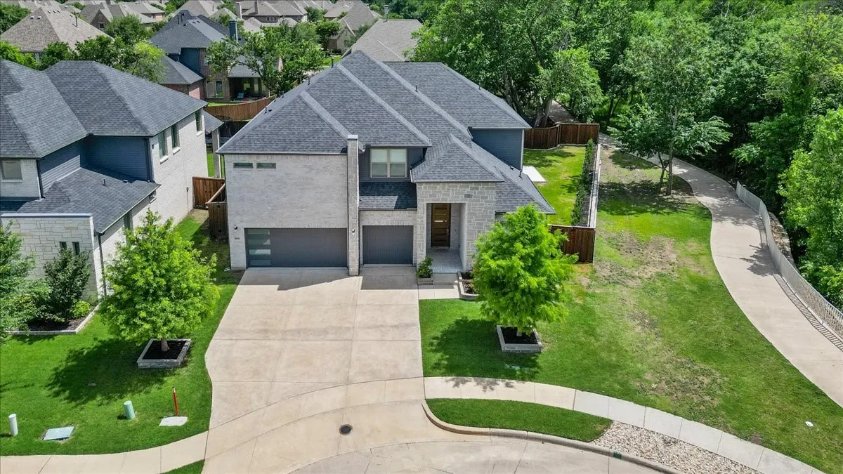Contemporary two-story residence featuring a stone and stucco exterior, dark gray shingle roof, and a concrete driveway
