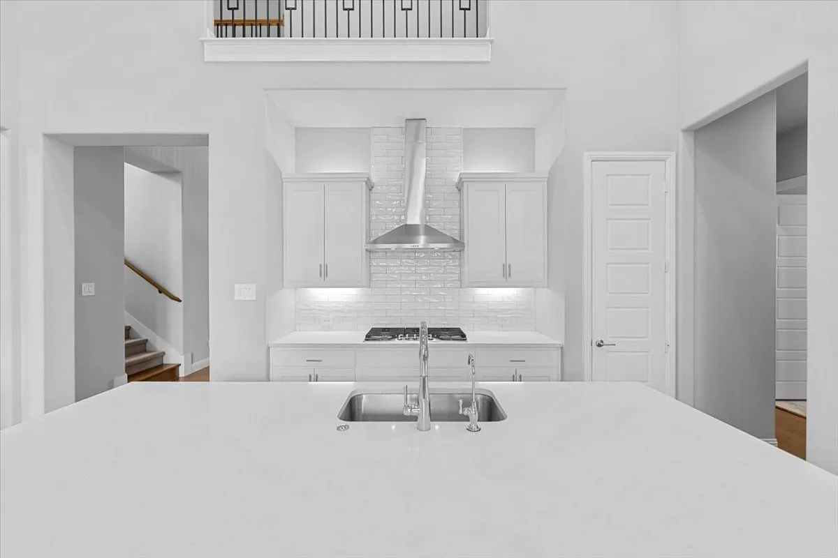 Modern kitchen featuring a large island with an undermount sink, white cabinetry, a gas range with a stainless steel vent hood, and a white subway tile backsplash