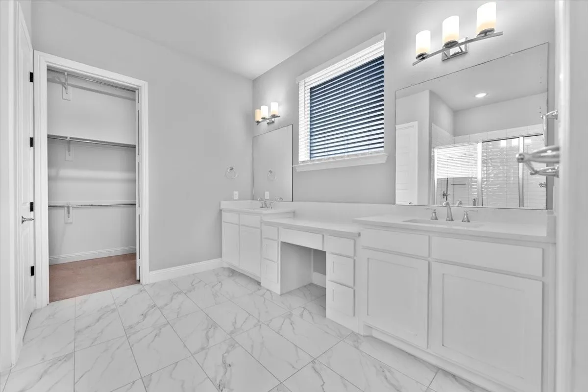 Spacious bathroom featuring marble-look tile flooring, dual white vanities with integrated sinks, a dedicated makeup counter, and a walk-in closet with built-in shelving