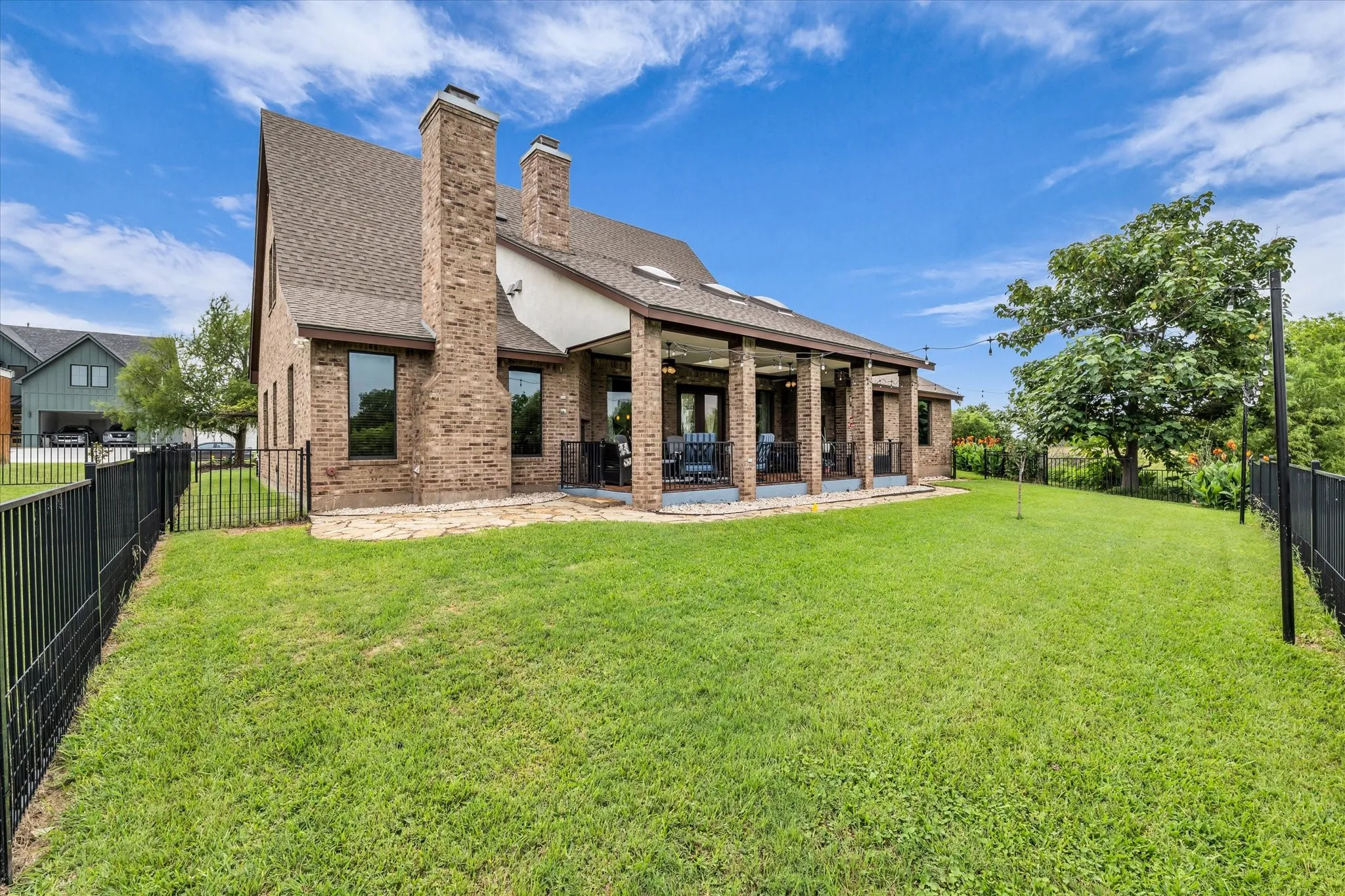 Expansive rear yard featuring green lawn, black iron fencing, and a covered patio
