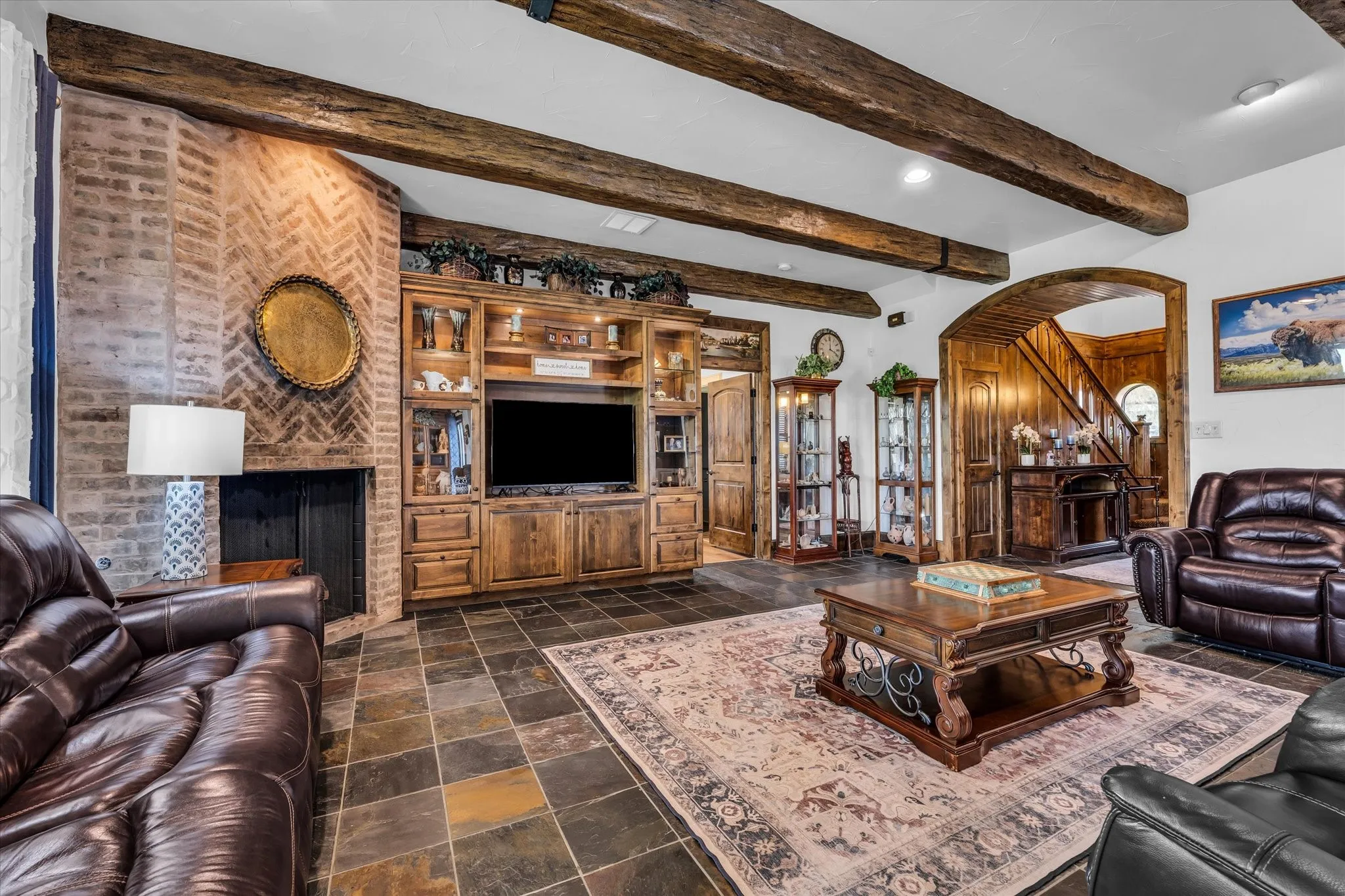 Living area featuring exposed wood ceiling beams, a herringbone brick fireplace, and a built-in entertainment center with display cabinets