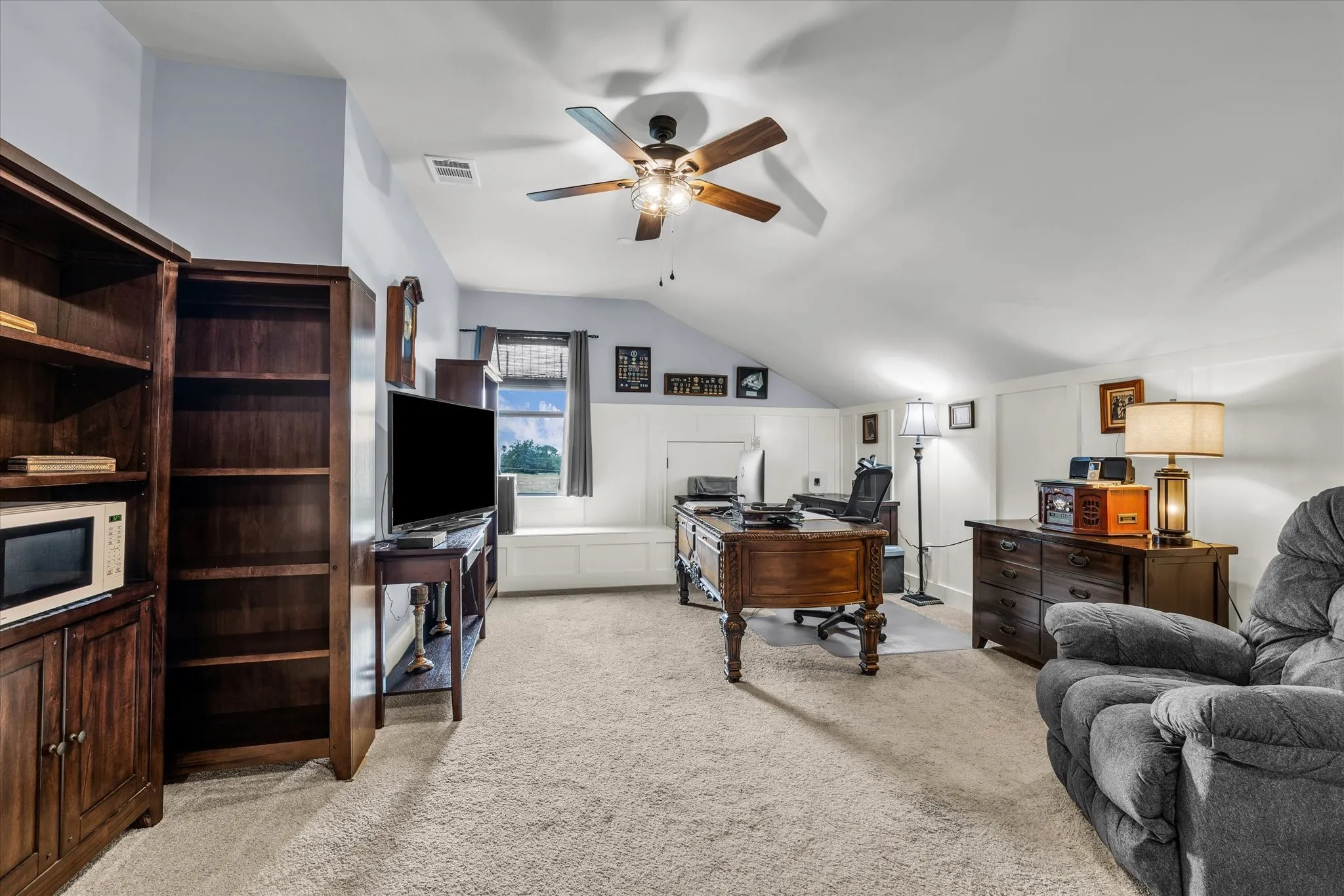Spacious bonus room featuring sloped ceilings, light-toned carpeting, a window with a built-in bench, and a ceiling fan