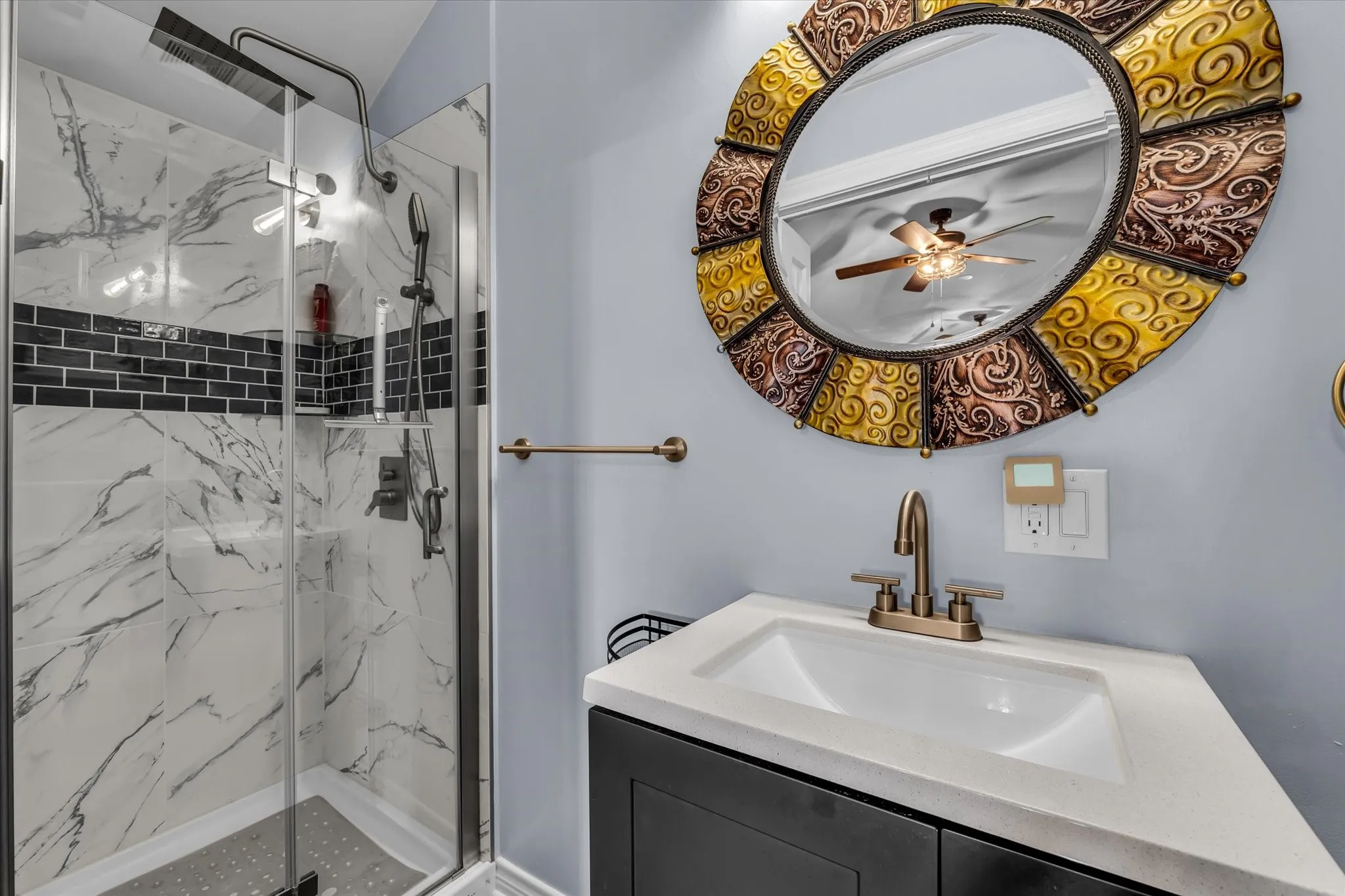 Walk-in shower with clear glass enclosure, marble-look tile, and black subway tile accent band