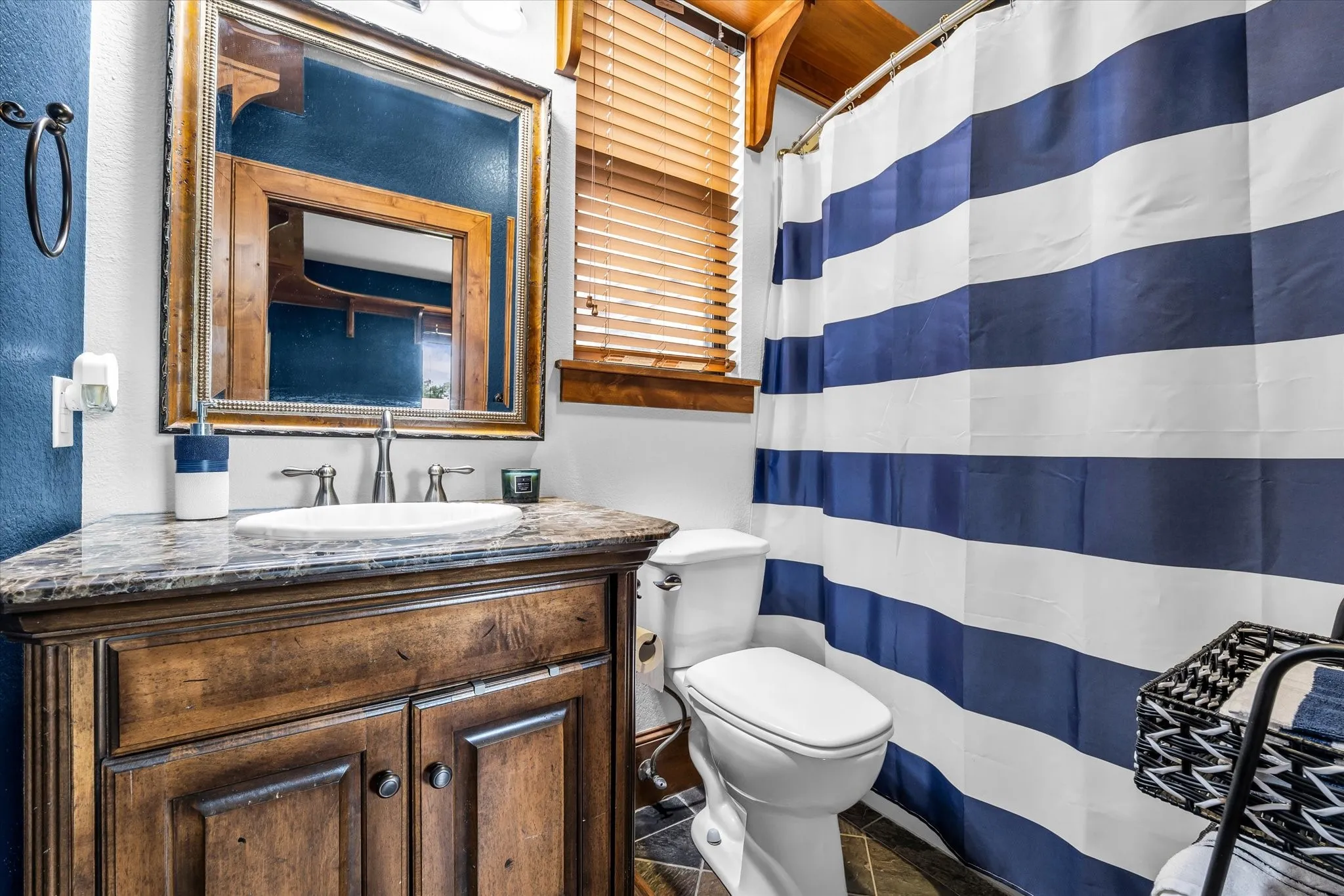 Bathroom featuring a wood-finish vanity with a stone countertop, an undermount sink, and an ornate framed mirror