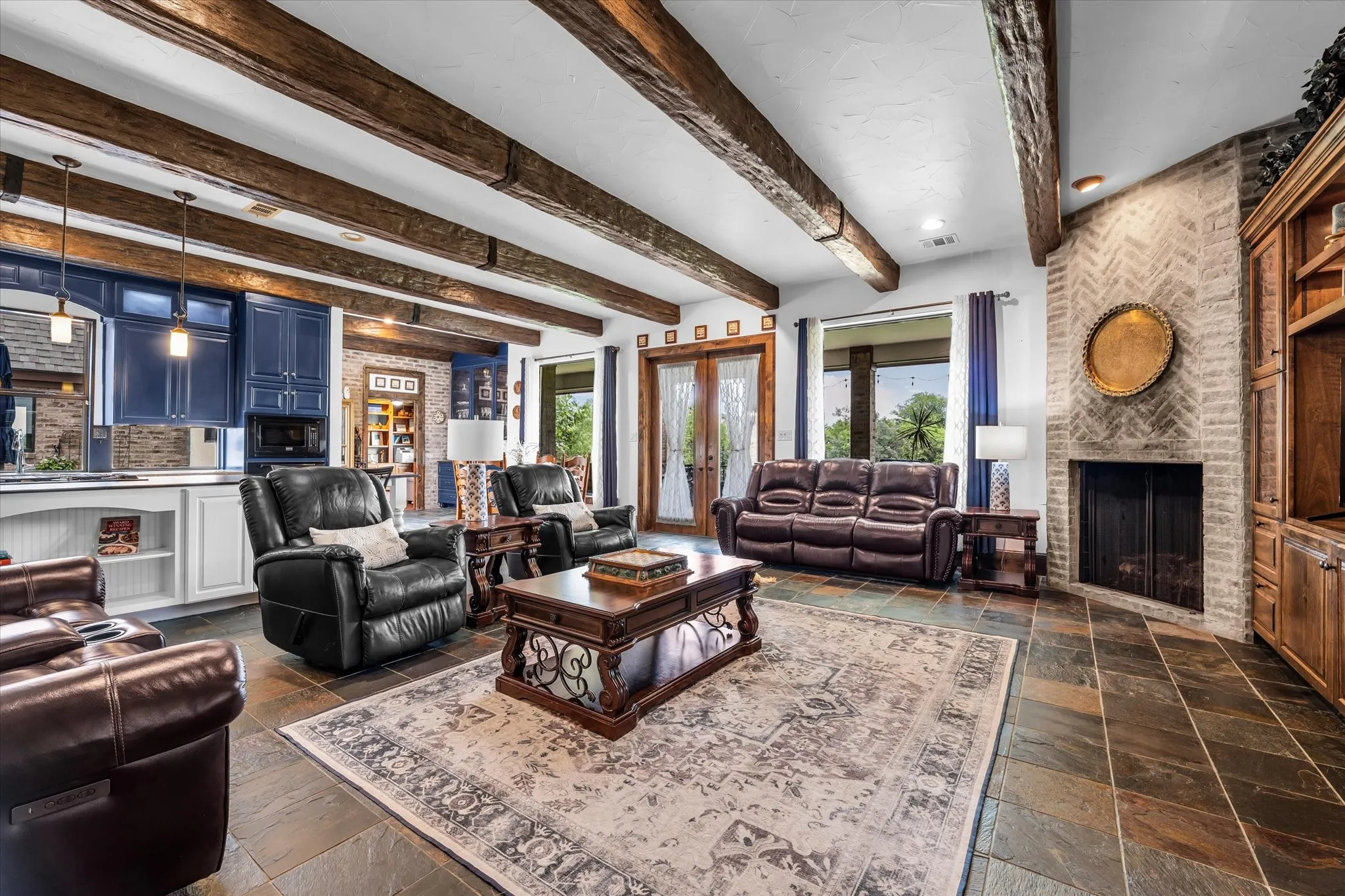 Spacious living area featuring exposed wood beams, slate tile flooring, a herringbone brick fireplace, and built-in cabinetry