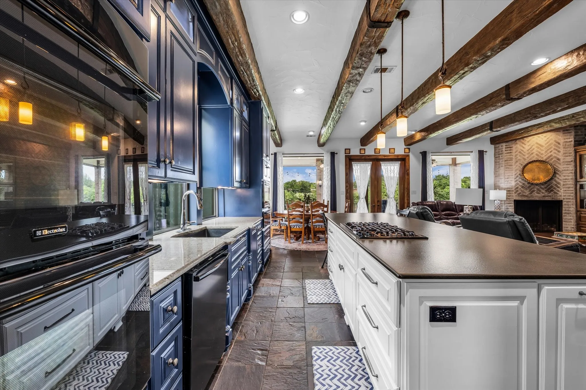 Open-concept kitchen featuring an oversized island with cooktop, blue and white cabinetry, recessed and pendant lighting, and slate tile flooring