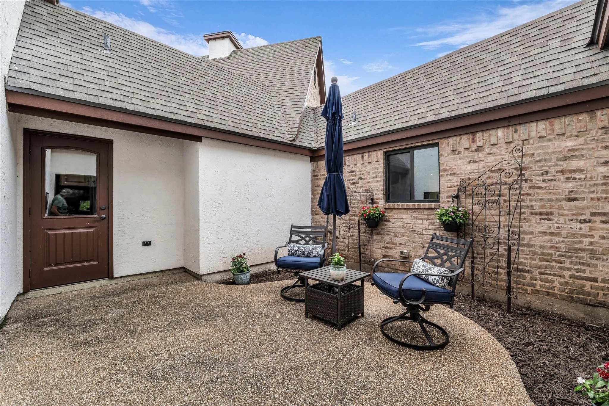 Outdoor patio featuring an exposed aggregate concrete surface, a brick exterior wall, and a white stucco exterior wall
