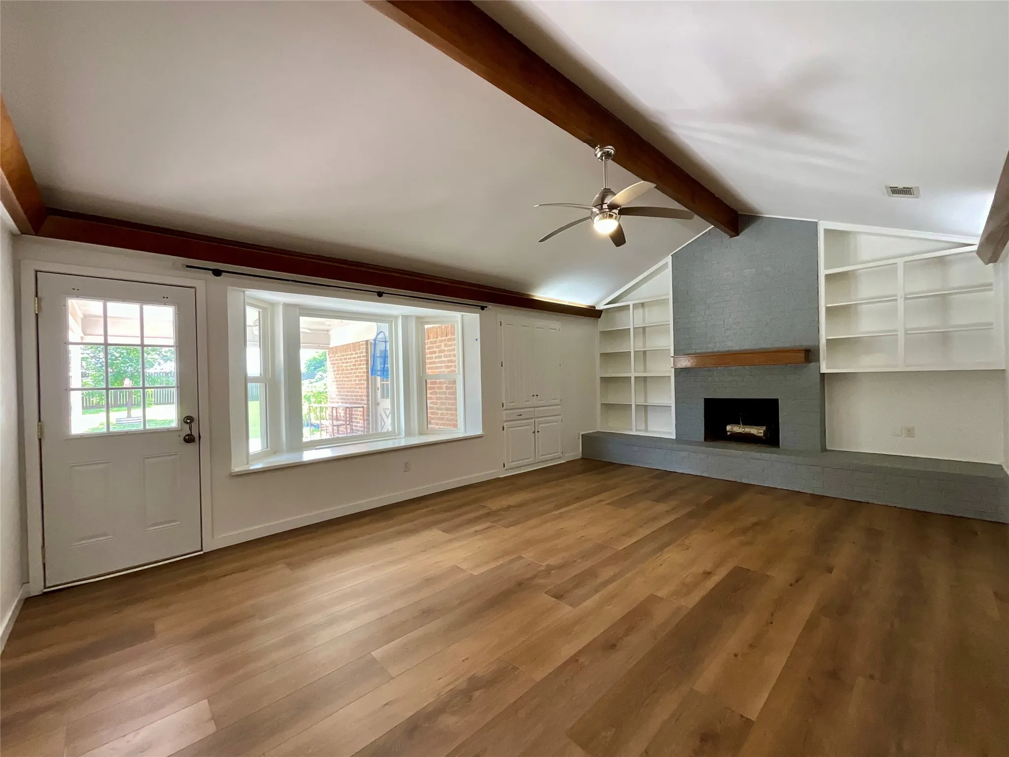 Vaulted ceiling living area featuring wood-finish flooring, exposed beams, and a ceiling fan