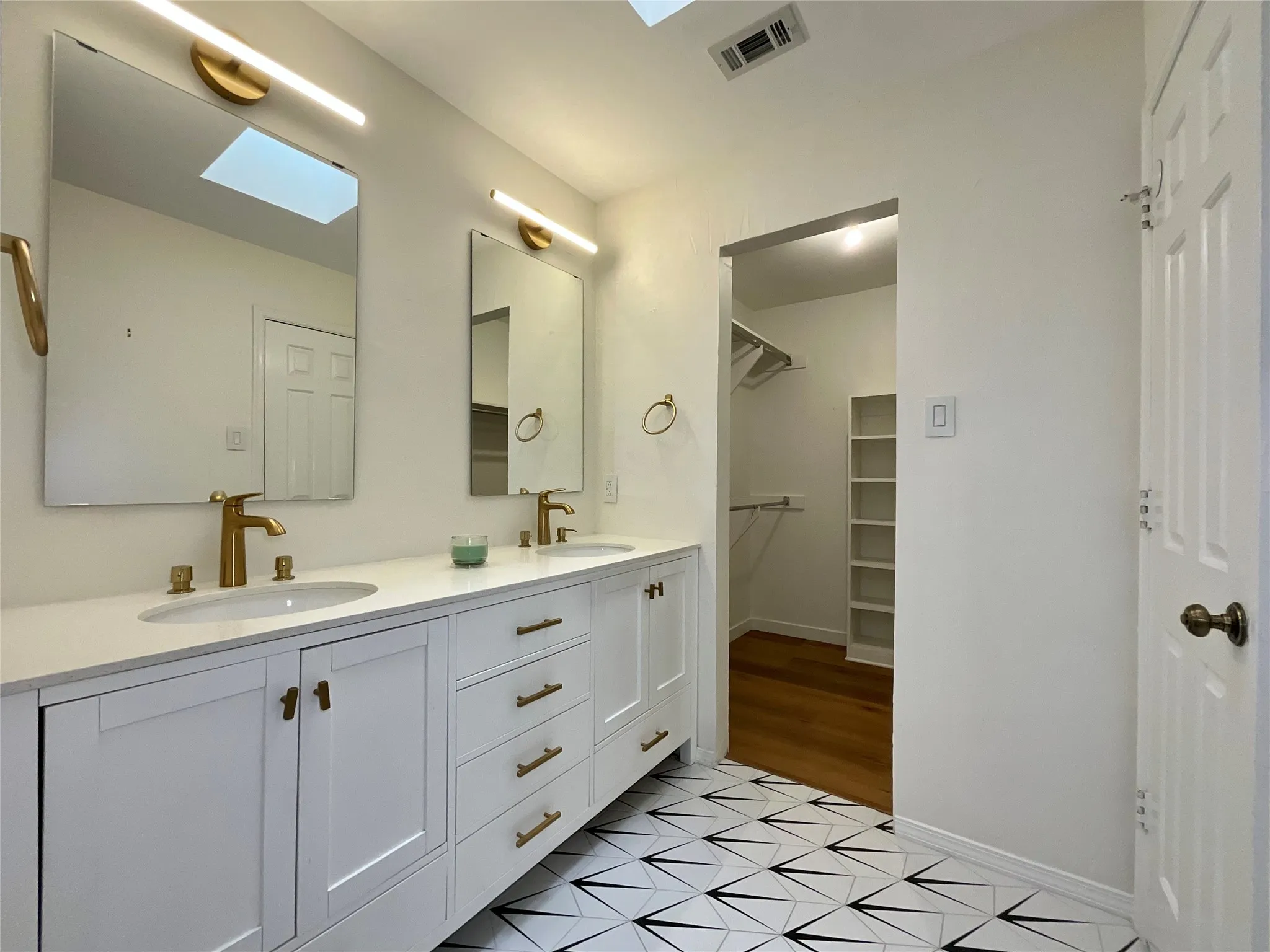 Bathroom featuring a double vanity with white cabinetry, gold-finish hardware, and a white countertop