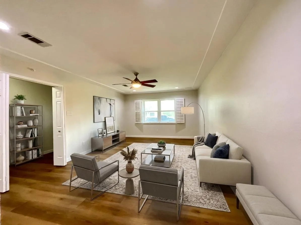 Spacious living area featuring wood-finish flooring, a ceiling fan with integrated lighting, and white plantation shutters