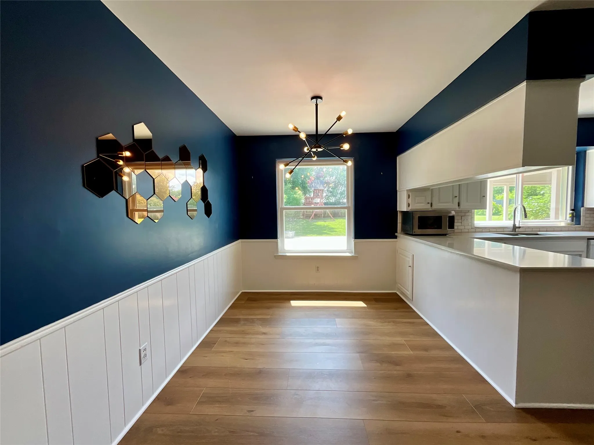 Open-concept dining area featuring wood-finish flooring, wainscoting, and a contemporary light fixture
