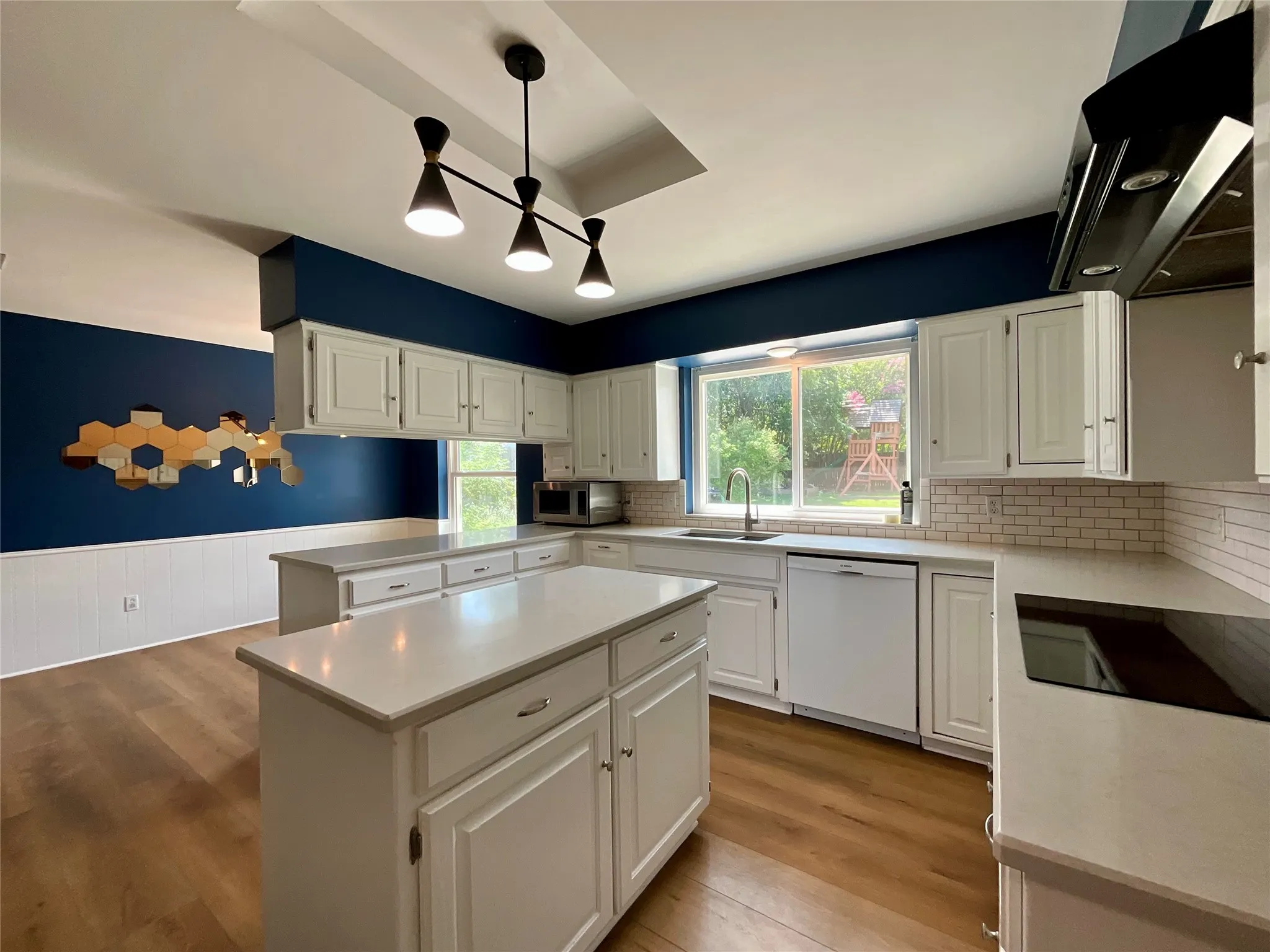Modern kitchen featuring a central island, white cabinetry, integrated appliances, and wood-finish flooring