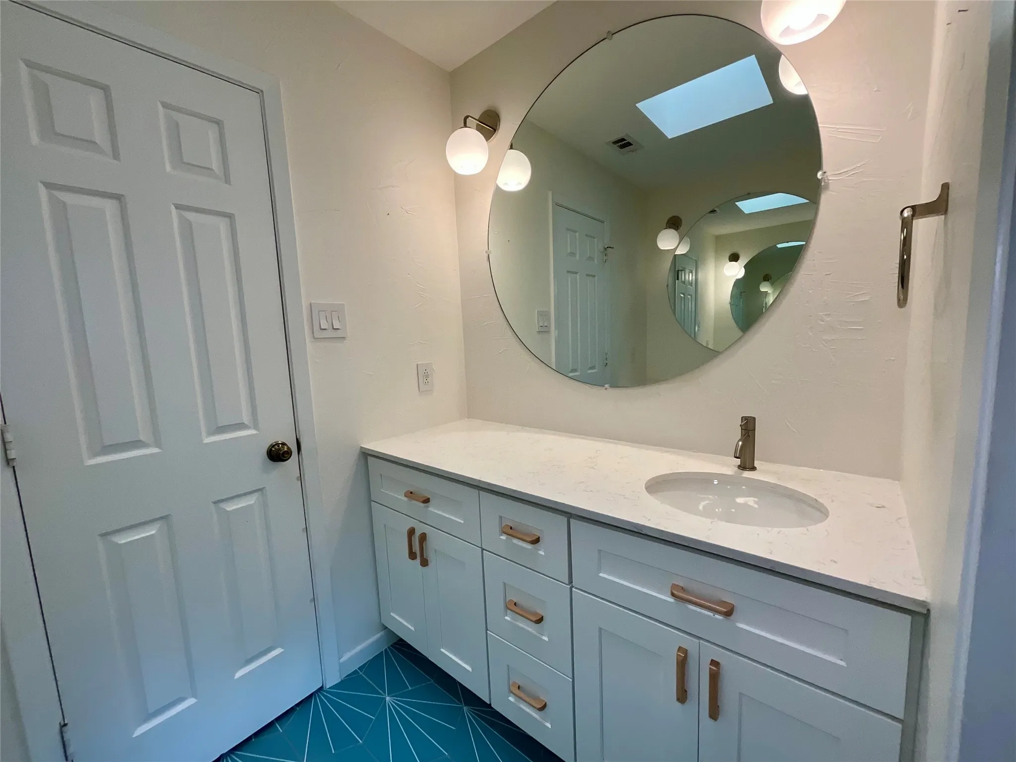 Modern vanity featuring a white countertop with an integrated sink, brushed brass faucet, and contemporary white cabinetry with matching hardware