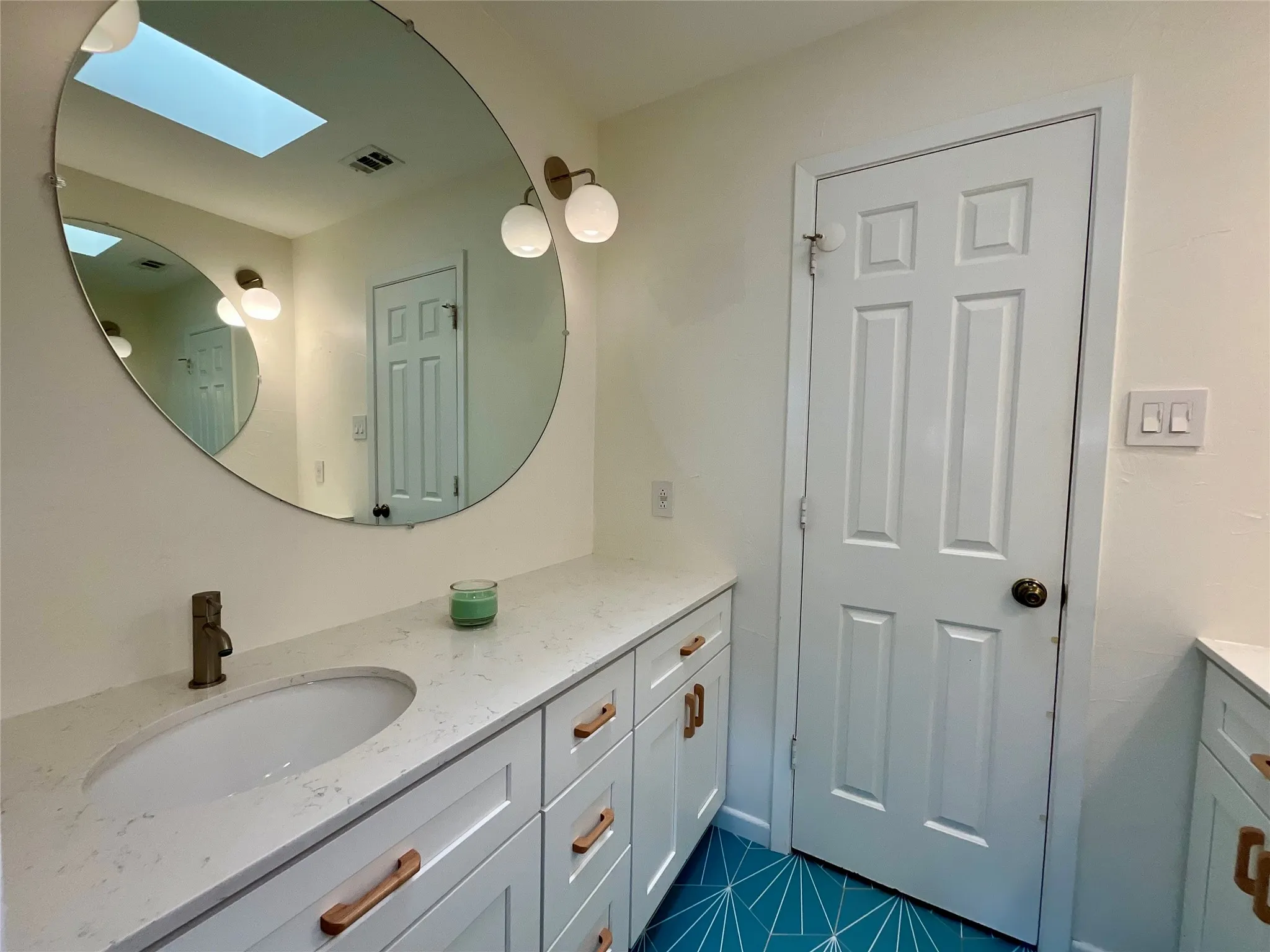 Modern vanity featuring white cabinetry with copper-toned pulls, a white oval undermount sink, and a quartz countertop
