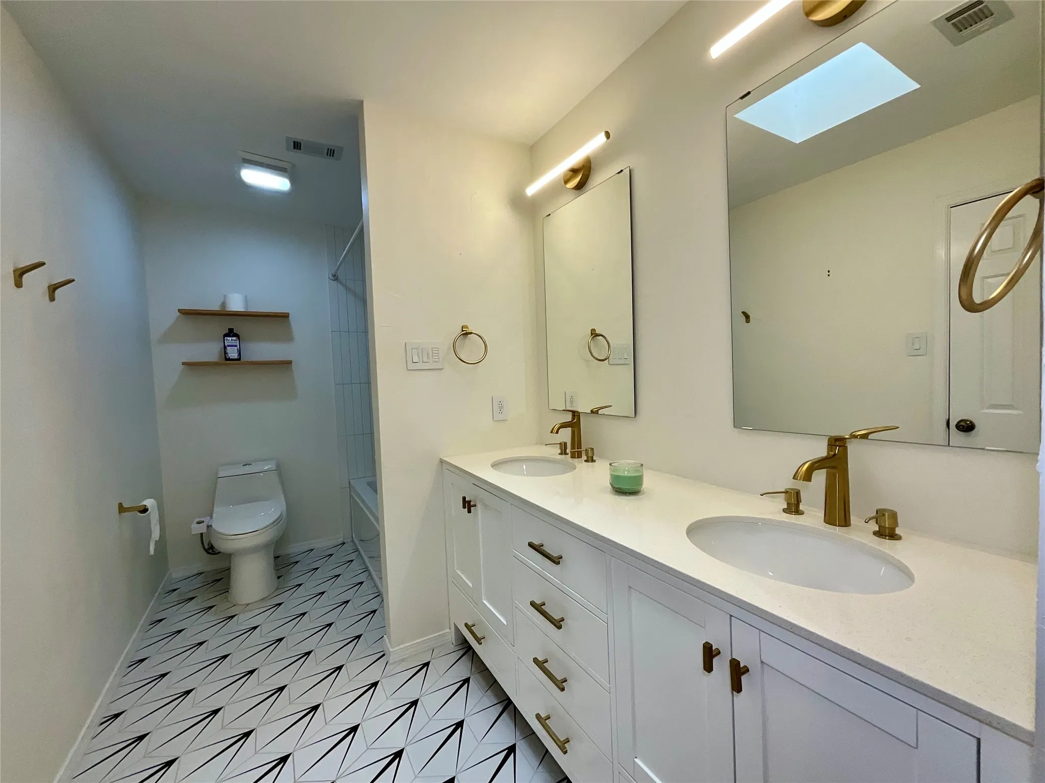 Contemporary bathroom featuring a double vanity with white cabinetry, gold-finish hardware, and a light-toned countertop