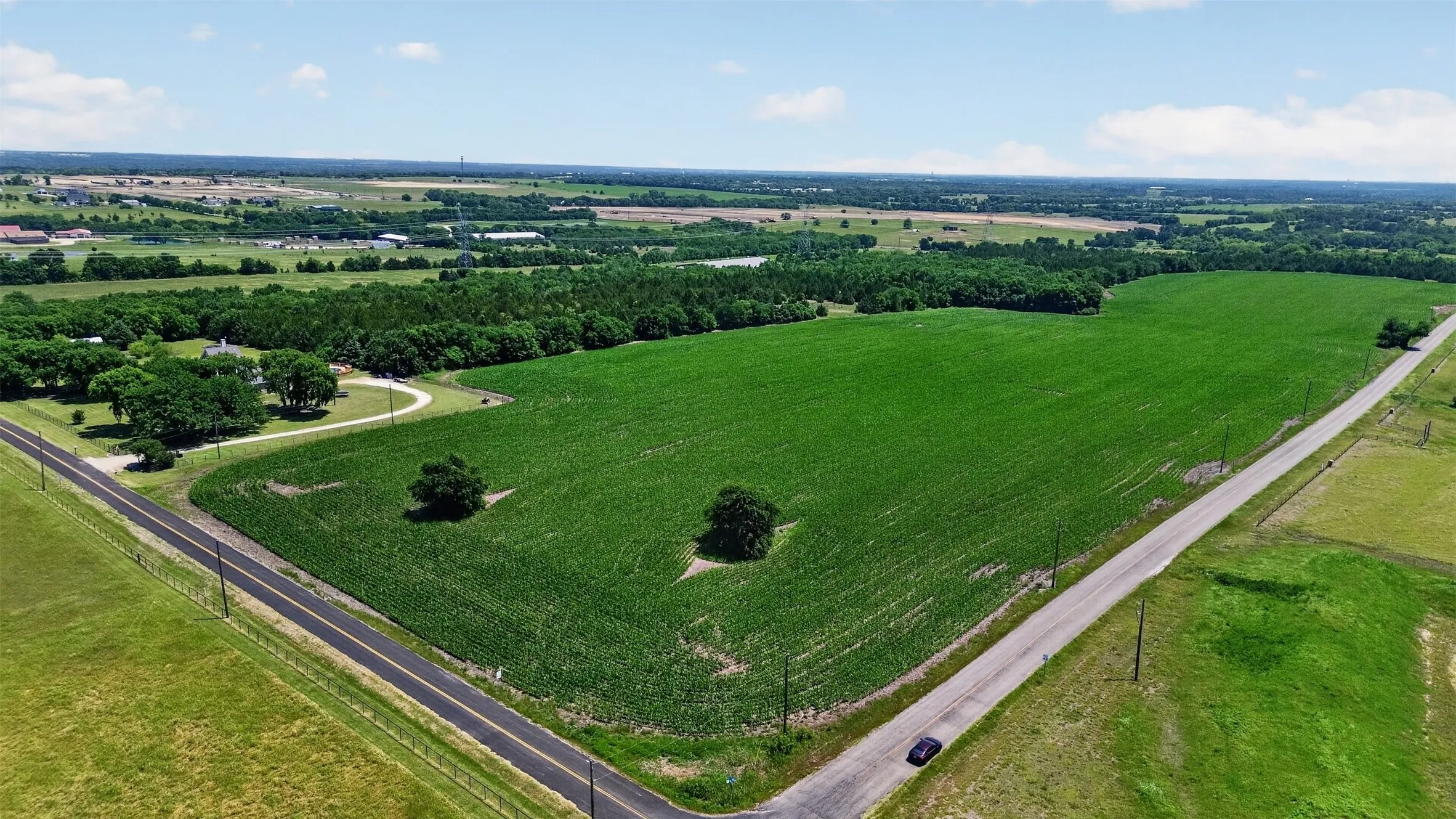 Expansive agricultural land featuring a verdant crop field, bordered by two paved roads