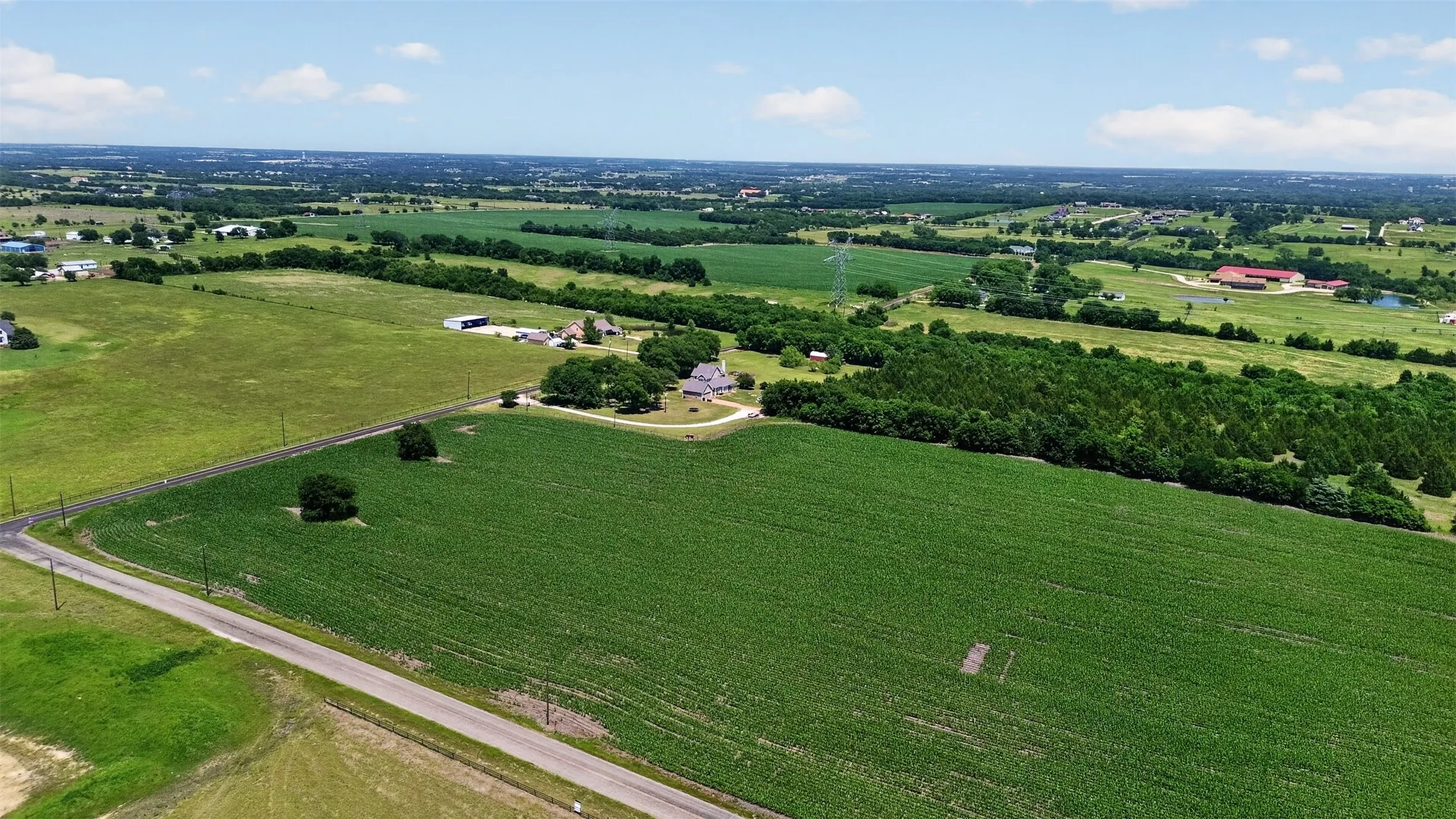 Expansive rural property featuring a main residence, surrounding green acreage, mature trees, and a paved road frontage