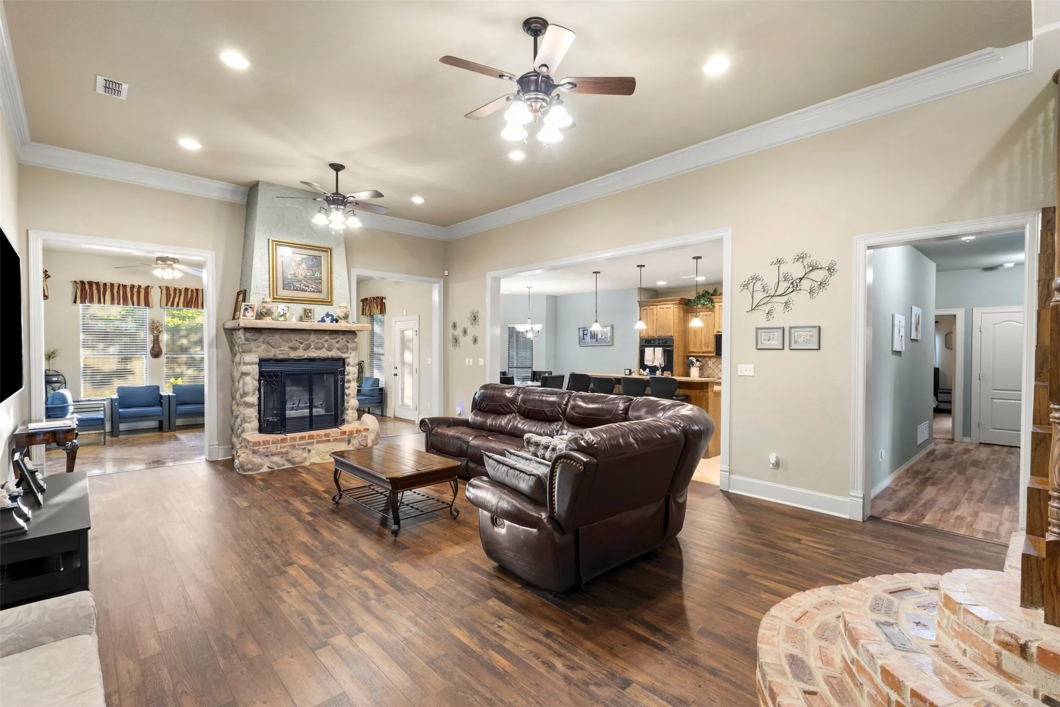 Living area with wood burning fireplace. Crown moulding, recessed lights, two ceiling fans, laminate floors. Fireplace is built with large river rock type stone.  Landing of stairs is made of bricks from various places.