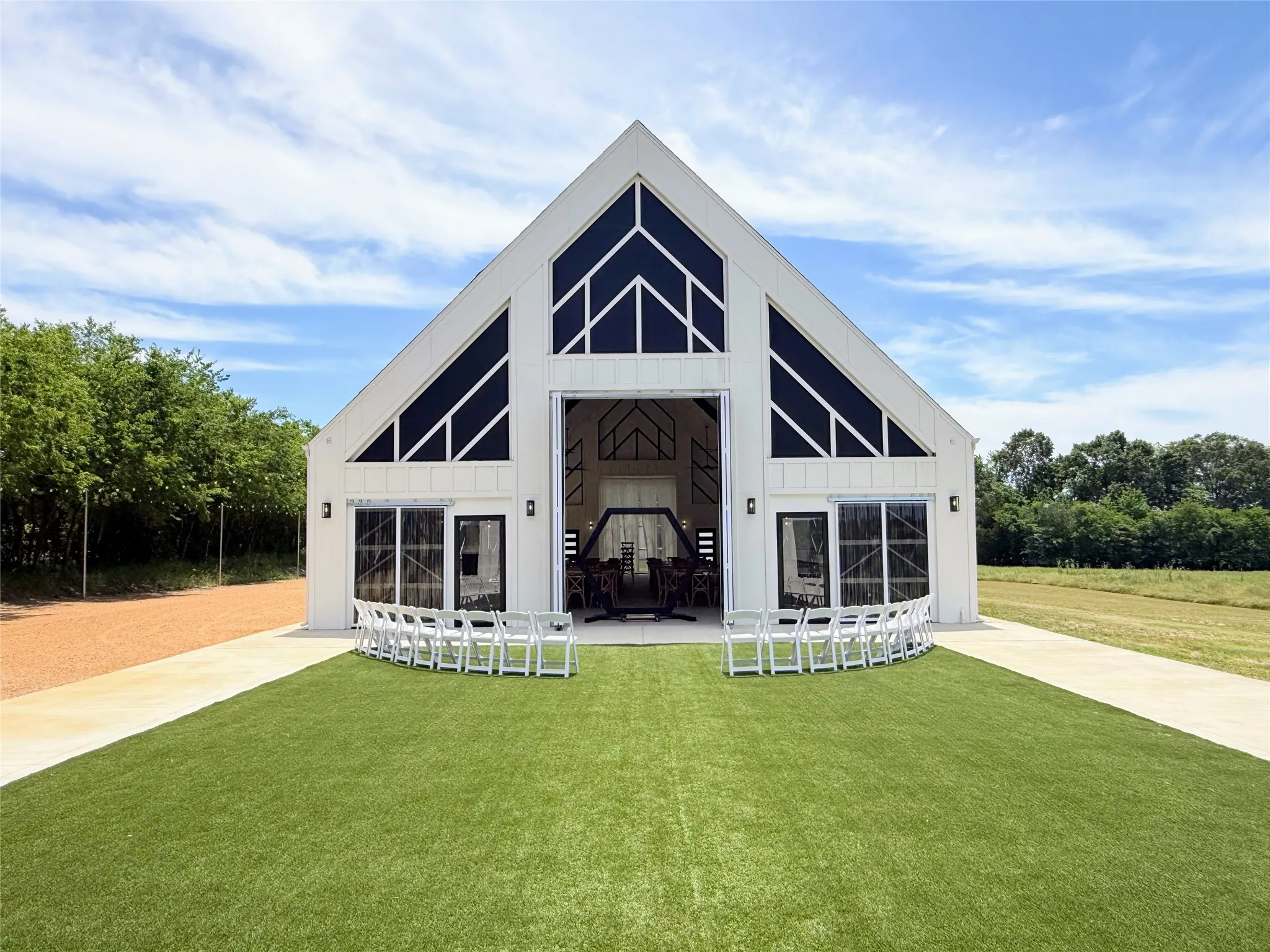 Modern barn-style structure with a white exterior, featuring a tall gabled roofline and prominent triangular window sections
