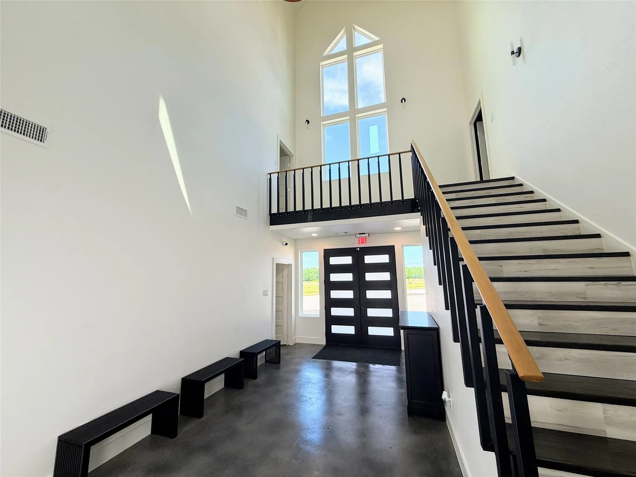 Two-story entryway featuring a prominent staircase with wood-finish treads and black risers, a second-story interior balcony with black railings, and a two-story window array