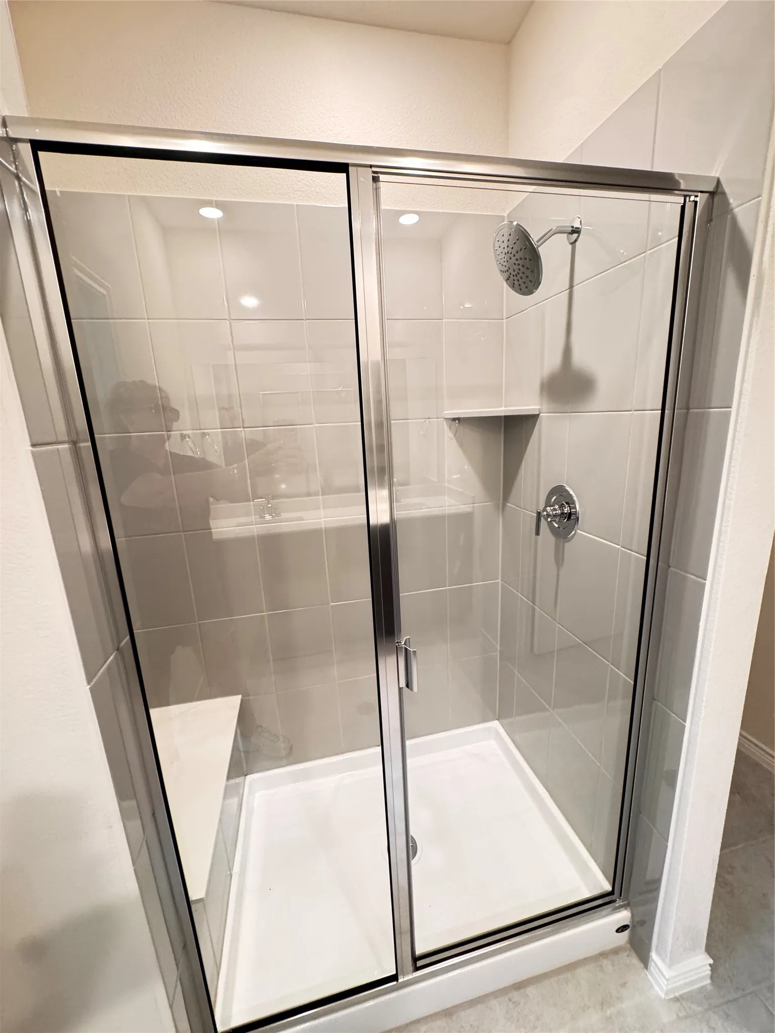 Enclosed shower with sliding glass doors, a built-in corner bench, and a rain shower head
