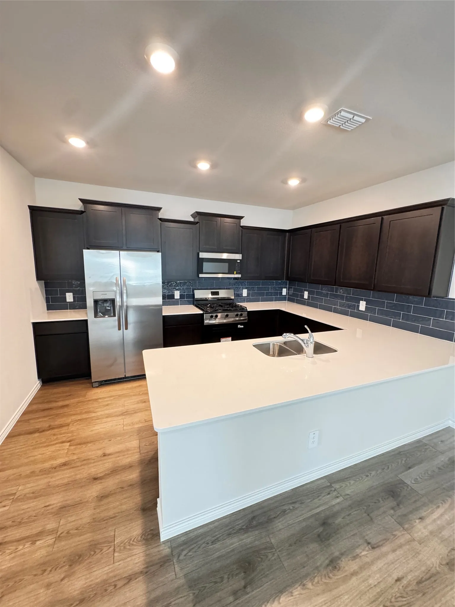 U-shaped kitchen featuring wood-finish flooring, dark wood cabinetry, and stainless steel appliances