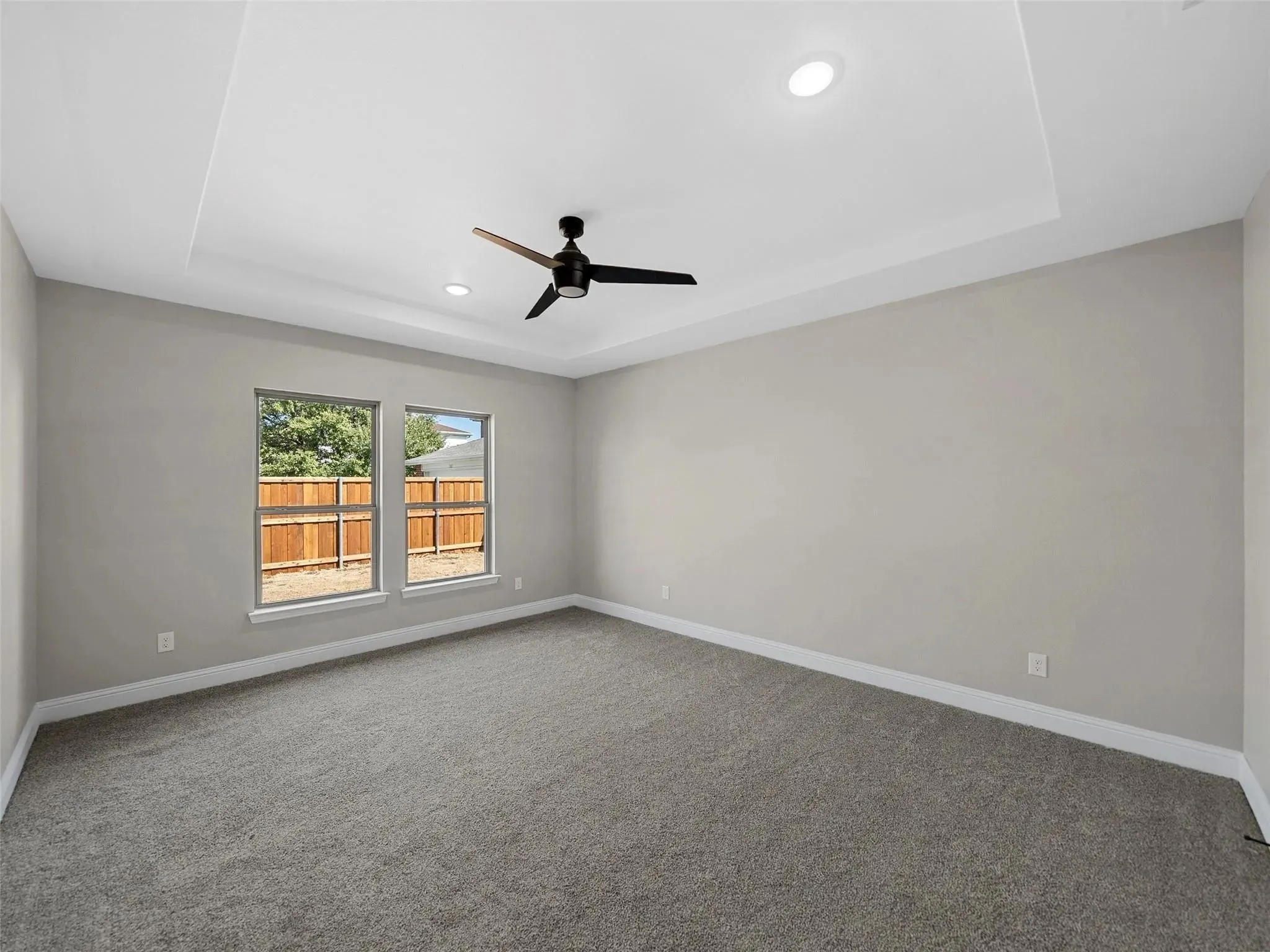 Spacious room featuring a tray ceiling with recessed lighting and a ceiling fan