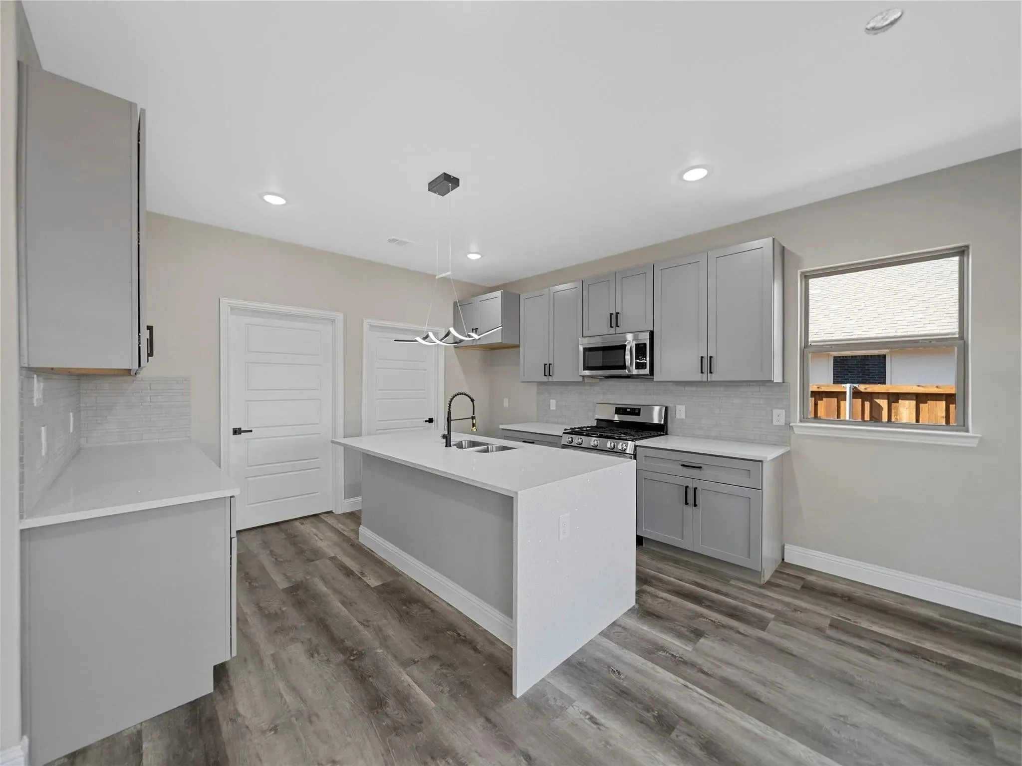 Kitchen featuring light gray cabinetry, quartz countertops, a center island with sink, stainless steel appliances, and wood-finish flooring