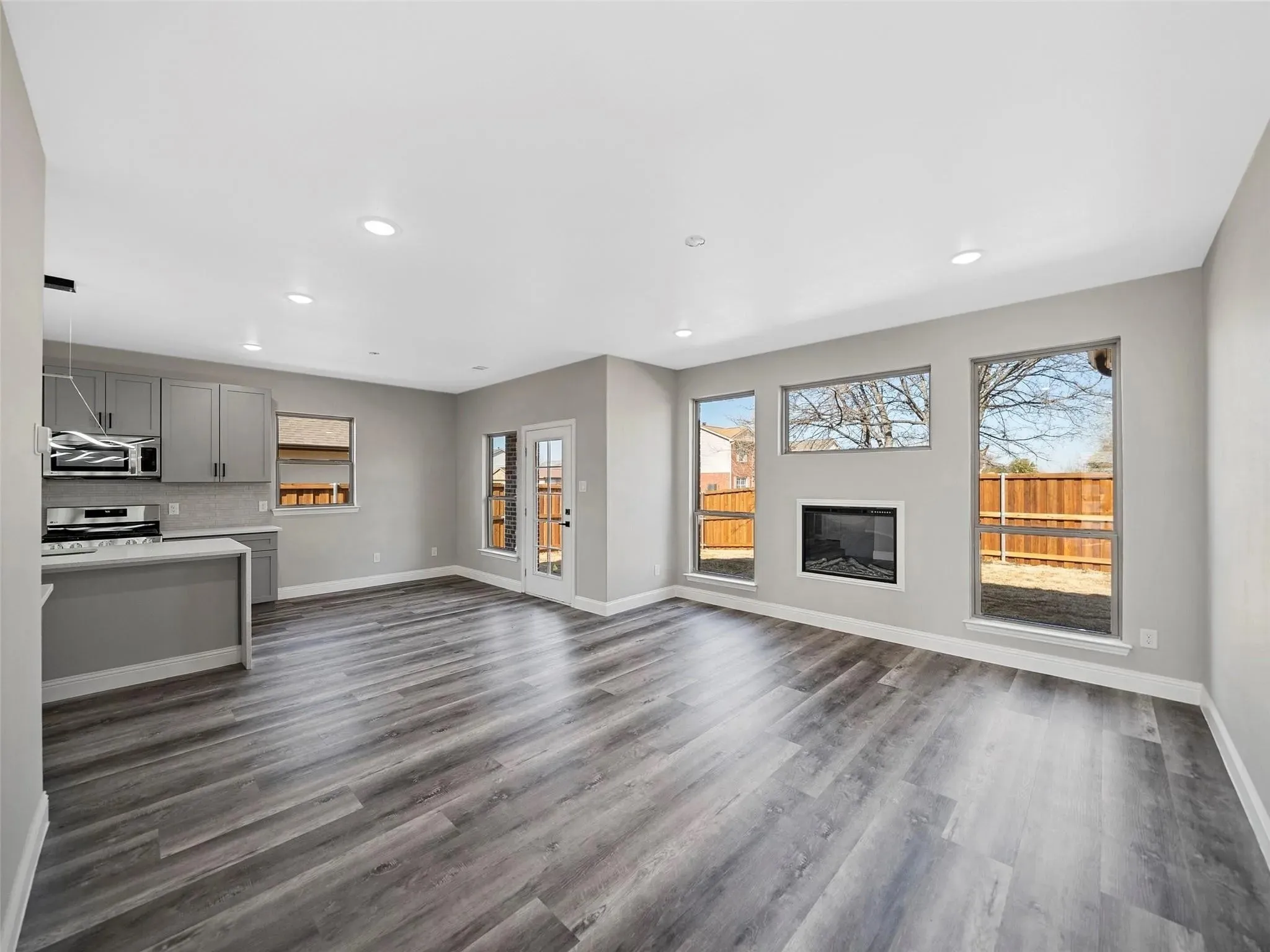 Open-concept living area featuring wood-finish flooring, a contemporary fireplace, recessed lighting, and expansive windows